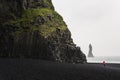 Woman in red raincoat taking pictures of the black basalt columns at the black sand beach in Vik, Iceland Royalty Free Stock Photo