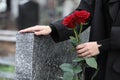 Woman with red roses near grey granite tombstone, closeup. Funeral ceremony Royalty Free Stock Photo