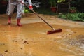 Woman in red rubber boots cleaning pavement covered in sand and water with red brush Royalty Free Stock Photo