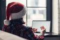 Woman in a red santa claus hat holding credit card using laptop for making order sitting near window. Christmas Royalty Free Stock Photo