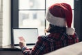 Woman in a red santa claus hat holding credit card using laptop for making order sitting near window. Christmas online shopping. Royalty Free Stock Photo