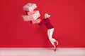 Woman in red santa claus hat trying to hold stack of gift boxes, on red studio background. Christmas shopping, copy space Royalty Free Stock Photo