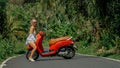 Woman on red scooter in white clothes drive on forest road trail. Dancing trip. One girl caucasian tourist in sunglasses