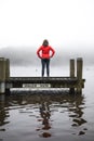 Woman in a red shirt overlooking the foggy scenery of the lake on a wooden pier Royalty Free Stock Photo