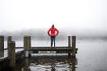 Woman in a red shirt overlooking the foggy scenery of the lake on a wooden pier Royalty Free Stock Photo