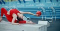 Woman in red sports costume performing callisthenics exercises with gymnastic ball at workout playground outdoors