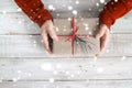 A woman in a red sweater holding a Christmas gift with a red ribbon and snow over on a wooden table. Royalty Free Stock Photo