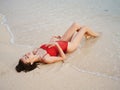 A woman in a red swimsuit lies on the sand with a beautiful tan body from the sun and looks into the ocean camera in the Royalty Free Stock Photo