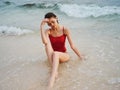 A woman in a red swimsuit sits on the sand with a beautiful sun tan and looks out at the ocean in the tropics on Bali Royalty Free Stock Photo