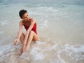 A woman in a red swimsuit sits on the sand with a beautiful sun tan and looks out at the ocean in the tropics on Bali Royalty Free Stock Photo