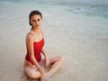 A woman in a red swimsuit sits on the sand with a beautiful sun tan and looks out at the ocean in the tropics on Bali Royalty Free Stock Photo