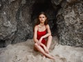 Woman in red swimsuit sitting by the rocks on the sand with a beautiful tan from the sun on the beach, travel to Bali, a Royalty Free Stock Photo