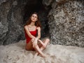 Woman in red swimsuit sitting by the rocks on the sand with a beautiful tan from the sun on the beach, travel to Bali, a Royalty Free Stock Photo