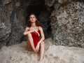 Woman in red swimsuit sitting by the rocks on the sand with a beautiful tan from the sun on the beach, travel to Bali, a Royalty Free Stock Photo