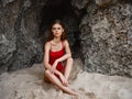 Woman in red swimsuit sitting by the rocks on the sand with a beautiful tan from the sun on the beach, travel to Bali, a Royalty Free Stock Photo