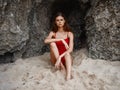 Woman in red swimsuit sitting by the rocks on the sand with a beautiful tan from the sun on the beach, a trip to the sea Royalty Free Stock Photo