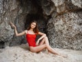 Woman in red swimsuit sitting by the rocks on the sand with a beautiful tan from the sun on the beach, a trip to the sea Royalty Free Stock Photo