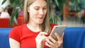 Woman in red t-shirt sitting in cafe using her smartphone, chatting with friends eating french fries