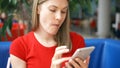 Woman in red t-shirt sitting in cafe using her smartphone, chatting with friends eating french fries