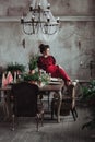 Woman in red vintage dress sits on the table served for christmas diner. Loft interior with clear concrete wall Royalty Free Stock Photo