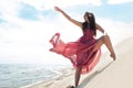 Woman in red waving dress with flying fabric runs on background of dunes. Royalty Free Stock Photo