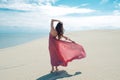 Woman in red waving dress with flying fabric runs on background of dunes. Royalty Free Stock Photo