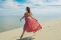 Woman in red waving dress with flying fabric runs on background of dunes. Skyline and the sea Royalty Free Stock Photo