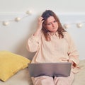 Woman reflected while sitting on the bed with a laptop. Sad girl with question on her face while working online from home