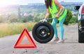 Woman in reflective vest holds wheel wrench and rolls the spare wheel. Spare wheel replacement. Punched wheel on the road while dr