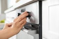 Woman regulating cooking mode on oven panel in kitchen