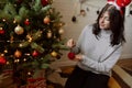 Woman in reindeer antlers decorating modern christmas tree with red bauble in festive room