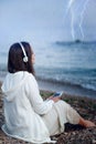 Woman relax listening music under rain, sitting on a sea beach.