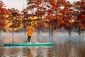 Woman relax on stand up paddle board at the lake with autumnal Taxodium trees in morning Royalty Free Stock Photo