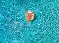 Woman relaxes on a donut shaped float over blue, sparkling pool water