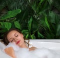 A woman relaxes in hot bath tub with soap foam