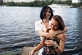 Two teenager girls sitting on a pier at the river bank having good time in summer. happy girl friends relaxing outdoor near lake.