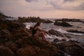 Woman relaxes on seaside rocks at dusk, legs dipped in splashing ocean waves, tranquil summer evening by the sea. Solo Royalty Free Stock Photo