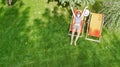 Woman relaxes in summer garden in sunbed deckchair on grass, young girl outdoors in green park on weekend, aerial drone view Royalty Free Stock Photo