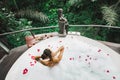 Woman relaxing bath tub full of foam outdoors with jungle view. View from behind Royalty Free Stock Photo