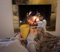 Woman relaxing by the fireplace warming up feet in woolen with a cup of hot drink socks and blanket Royalty Free Stock Photo