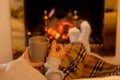 Woman relaxing by the fireplace warming up feet in woolen with a cup of hot drink socks and blanket Royalty Free Stock Photo