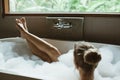 Woman relaxing in foam bath with bubbles in dark bathroom by window