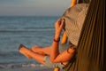 Woman relaxing on hammock with hat sunbathing on vacation. Against the background of the sea in the setting sun.