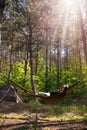 Woman relaxing in the hammock in the middle of a pine forest, watching sundown. Slow life concept. Hipster. Camping tent. Vertical