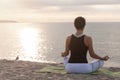 Woman relaxing in lotus pose on the beach. Meditation near the sea at sunrise