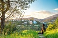 Woman relaxing and meditating at sunset on green hill with beautiful view of countryside and mountains