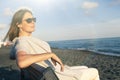 Woman relaxing at the sea dressed in peace sitting on the bench on the beach. Sunglasses Royalty Free Stock Photo