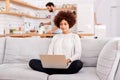 Woman Relaxing Sitting On Sofa At Home Using Laptop Computer With Man In Kitchen Pouring Drink Royalty Free Stock Photo