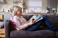 Woman Relaxing On Sofa Reading Newspaper In Modern Apartment Royalty Free Stock Photo