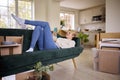 Woman Relaxing On Sofa Using Mobile Phone Surrounded By Unpacking Boxes After Moving Into New Home Royalty Free Stock Photo